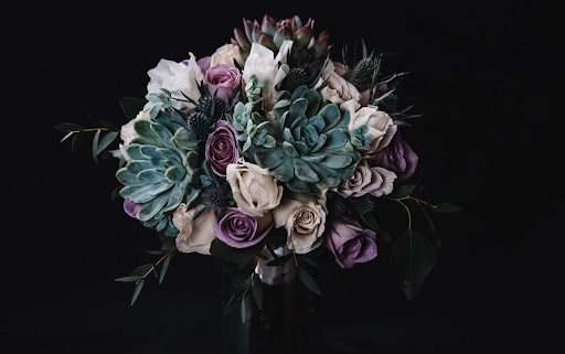 Floral arrangement photographed indoors by a professional photographer. The bouquet is made with roses, succulents, thistle, gunni eucalyptus. Succulents are wired with floral recipe instructions to ensure succulents do not fall out of the bouquet.